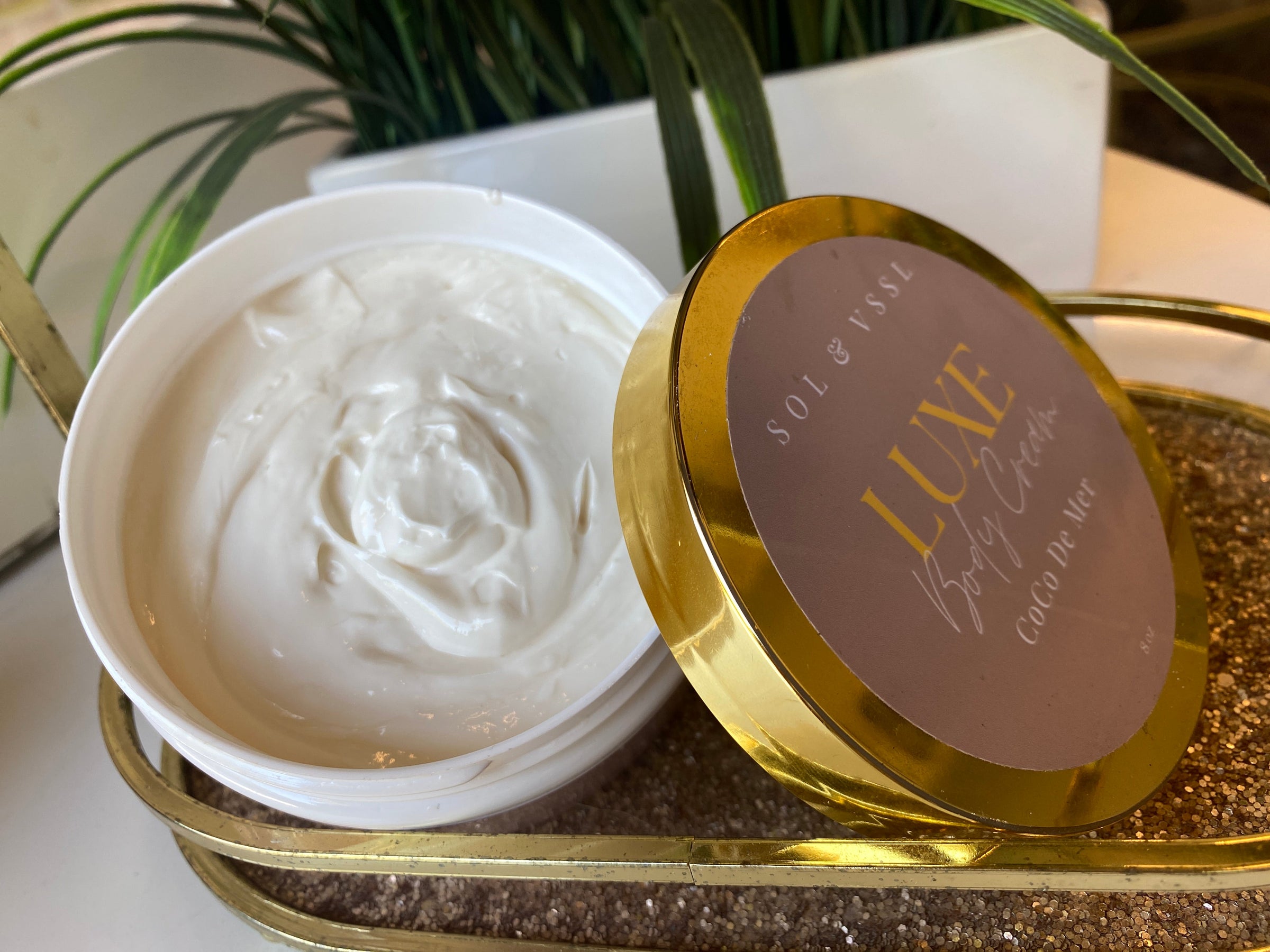 Luxe Body Cream Tub on a Table in front of plant