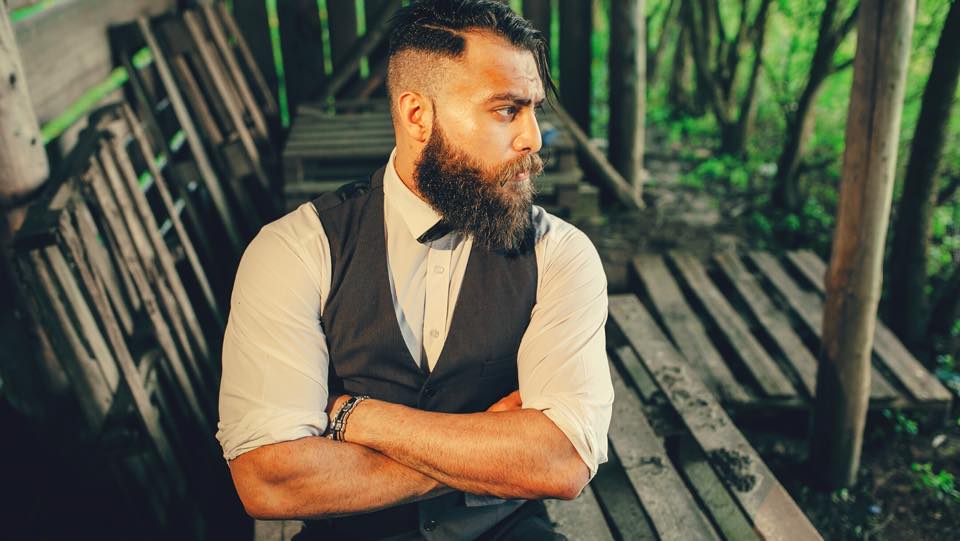 Dapper man with a large beard and clean haircut wearing a shirt and vest.